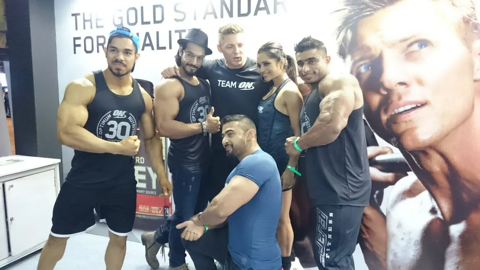 Six people in athletic wear posing together in front of a large exhibition backdrop.