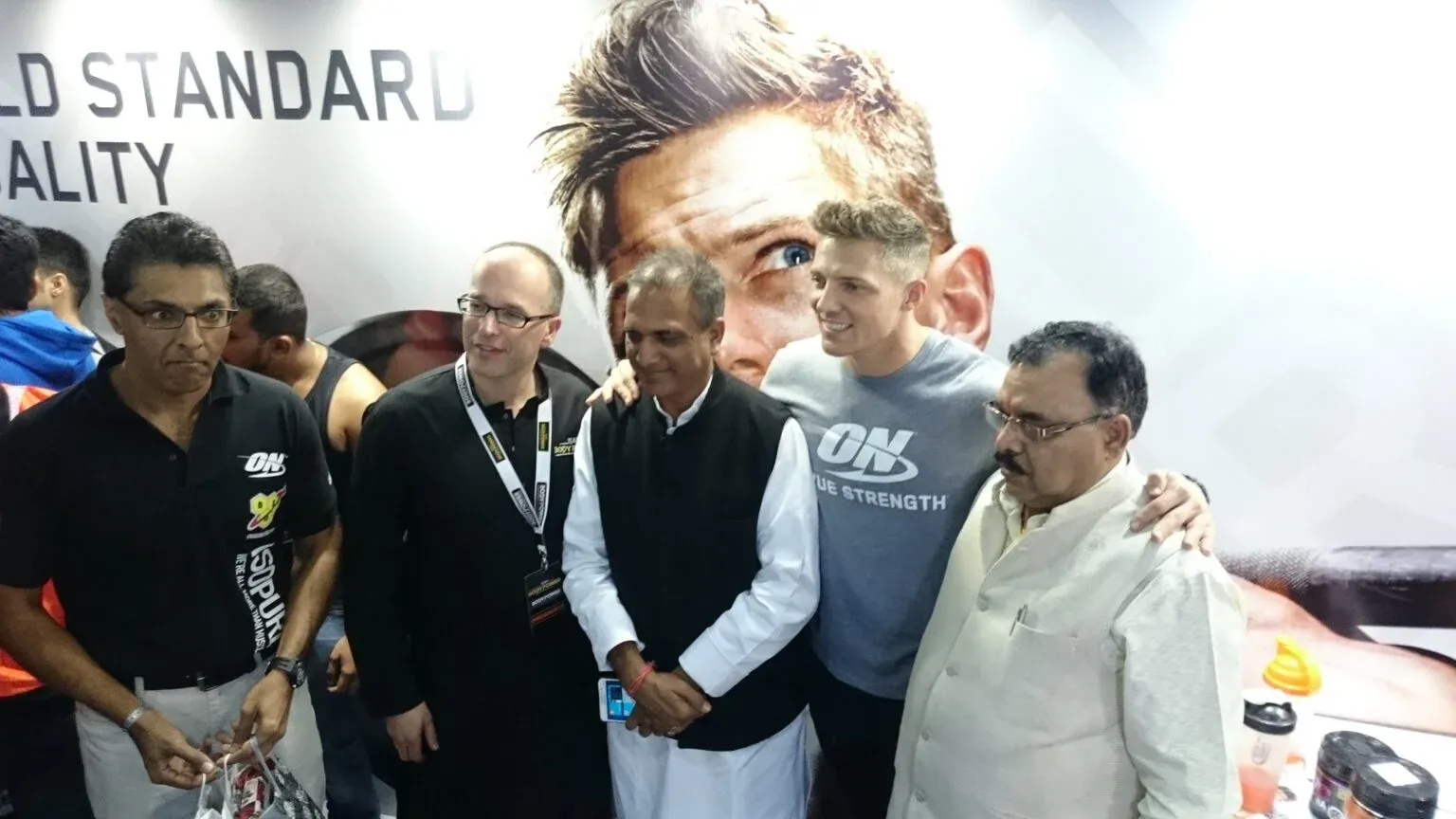 Five people standing together in front of a large promotional wall at an indoor exhibition.