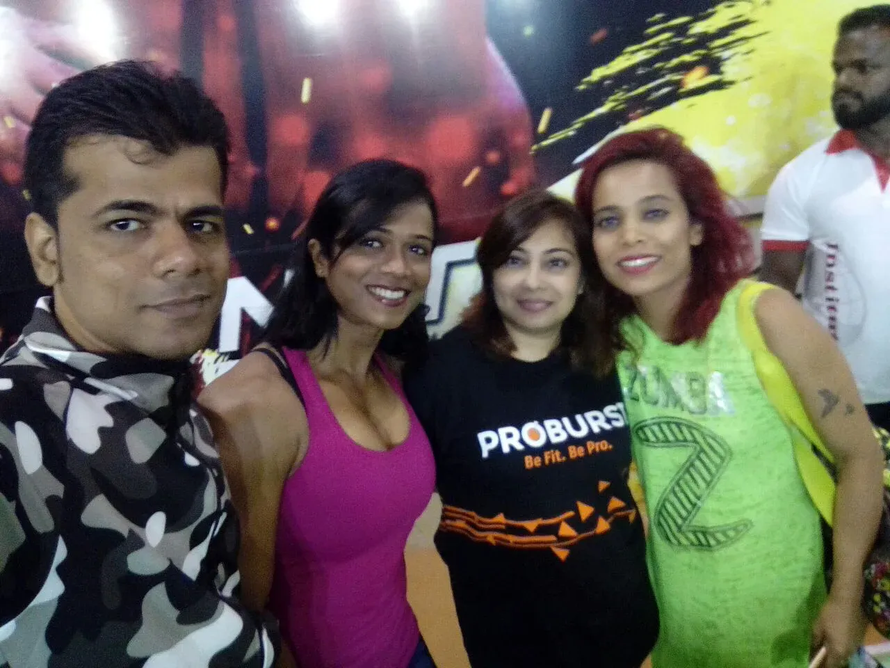 Four people smiling for a casual group photo in front of a colourful indoor backdrop.
